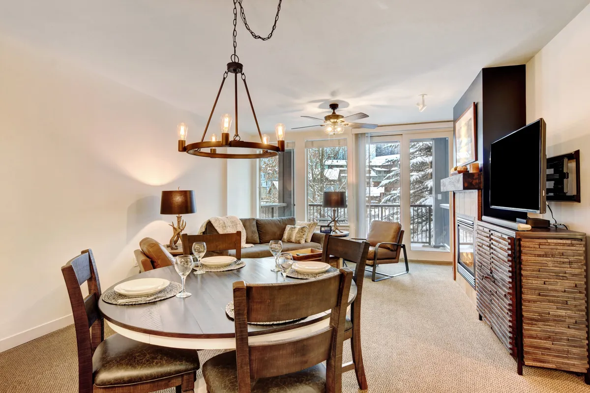 A broader view of the open-concept living area showing a plush sofa, a dining table with chairs, a striking fireplace, and expansive windows filling the space with natural light. The setup suggests a space ideal for board games, movie nights, or simply enjoying the view.
