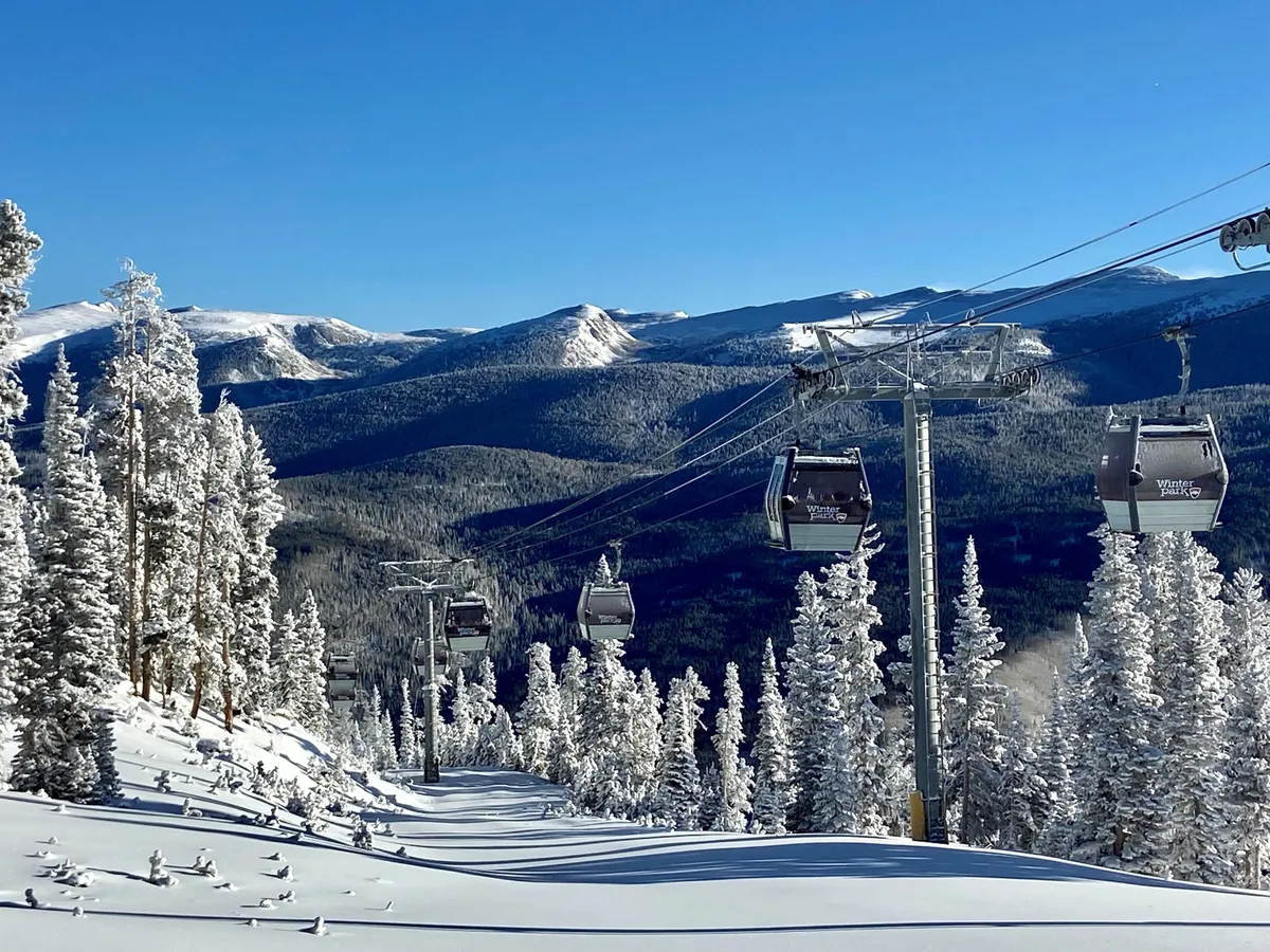 This image showcases ski lift gondolas gliding above a snowy landscape with snow-covered trees and expansive mountain ranges in the distance. The scene is serene yet invigorating, perfectly capturing the excitement and beauty of ski-in/ski-out access, while subtly hinting at the adventure and ease of hitting the slopes straight from the property.