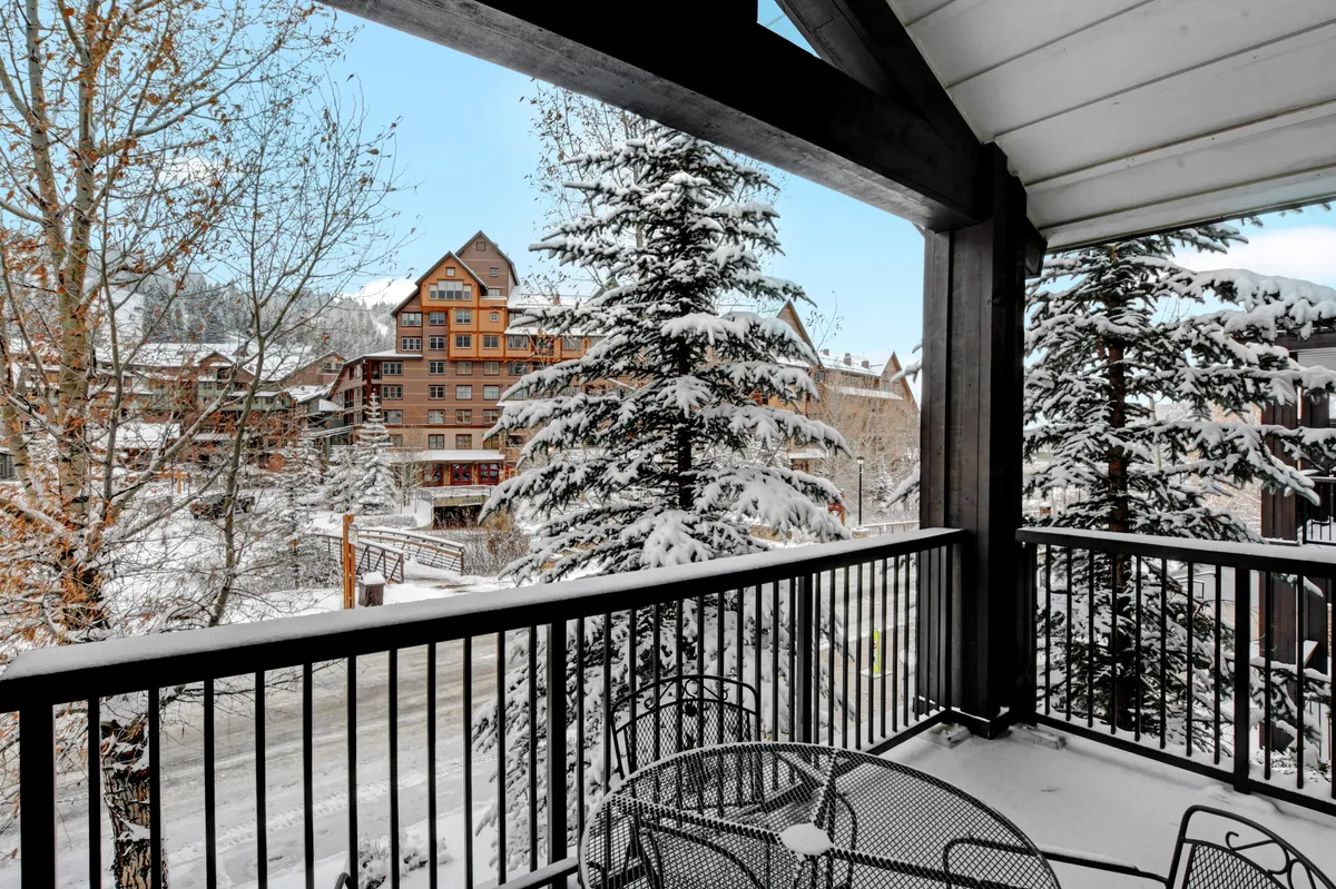 A peaceful winter scene featuring snow-covered trees and mountain views, with charming architectural details of nearby buildings. The image evokes the serene beauty of Winter Park during colder months, perfect for winter sports or cozying up after an adventure.