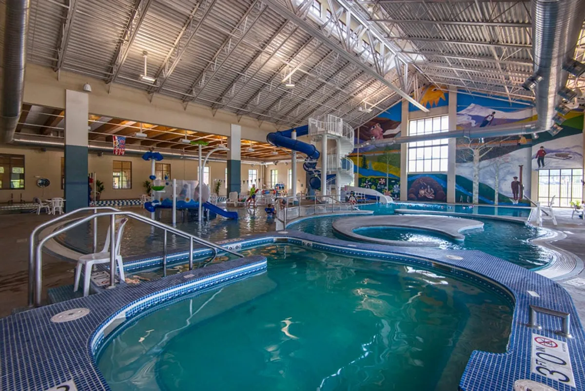 A bright and energetic interior scene of a recreational center featuring colorful murals, twisting water slides, a swimming pool, and children joyfully playing. The space radiates fun and is clearly tailored for families and year-round enjoyment.