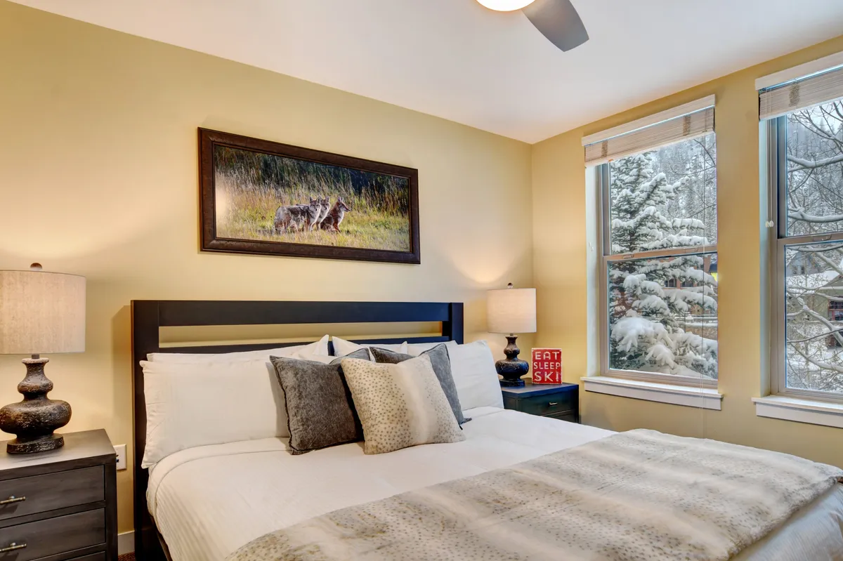 A tranquil bedroom with a neatly made bed, nightstands with lamps, large windows letting in natural light, and tasteful wall art. The space exudes comfort and relaxation, ideal for restful sleep.