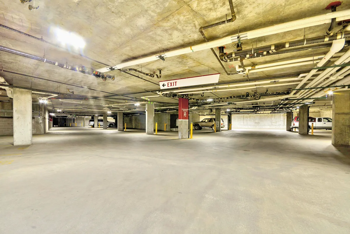 A well-lit underground parking garage featuring parking spaces, illuminated EXIT signage, support columns, and easy access points for guests. The design emphasizes convenience and security for guests arriving with plenty of gear.